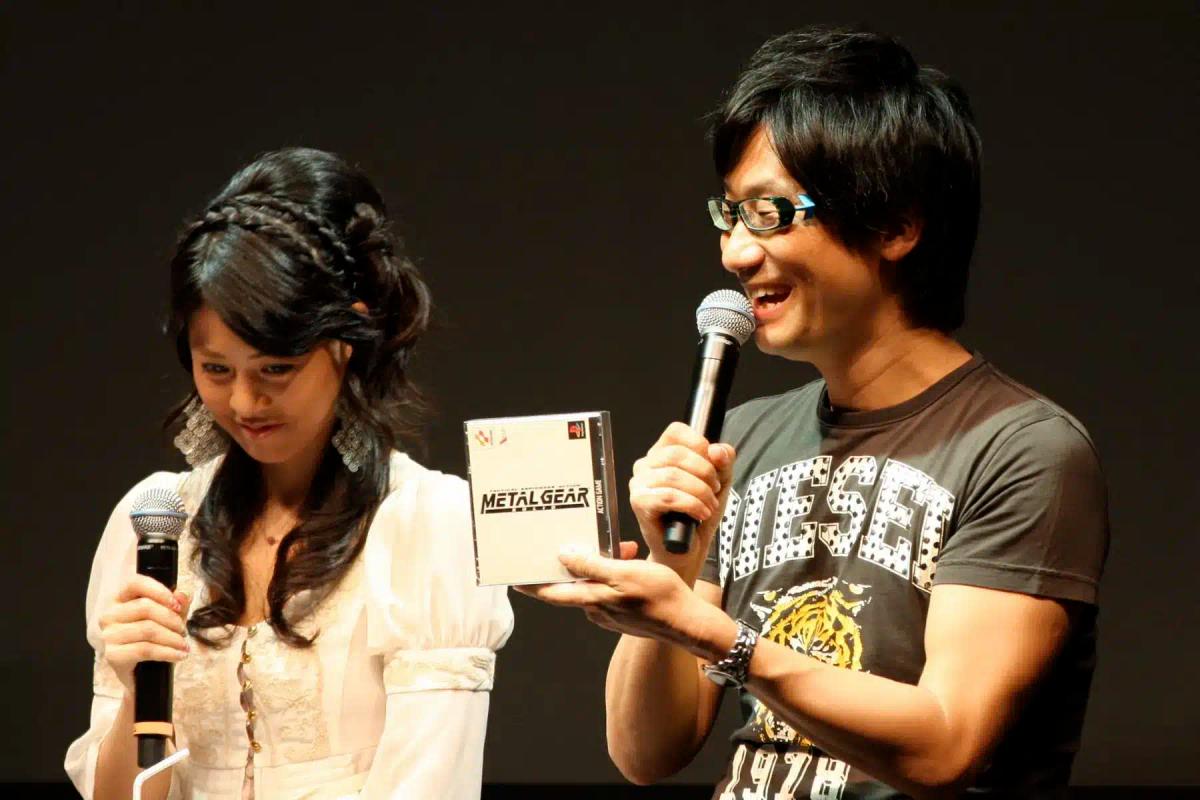 Hideo Kojima tiene in mano la custodia di un gioco di Metal Gear mentre parla in un microfono.